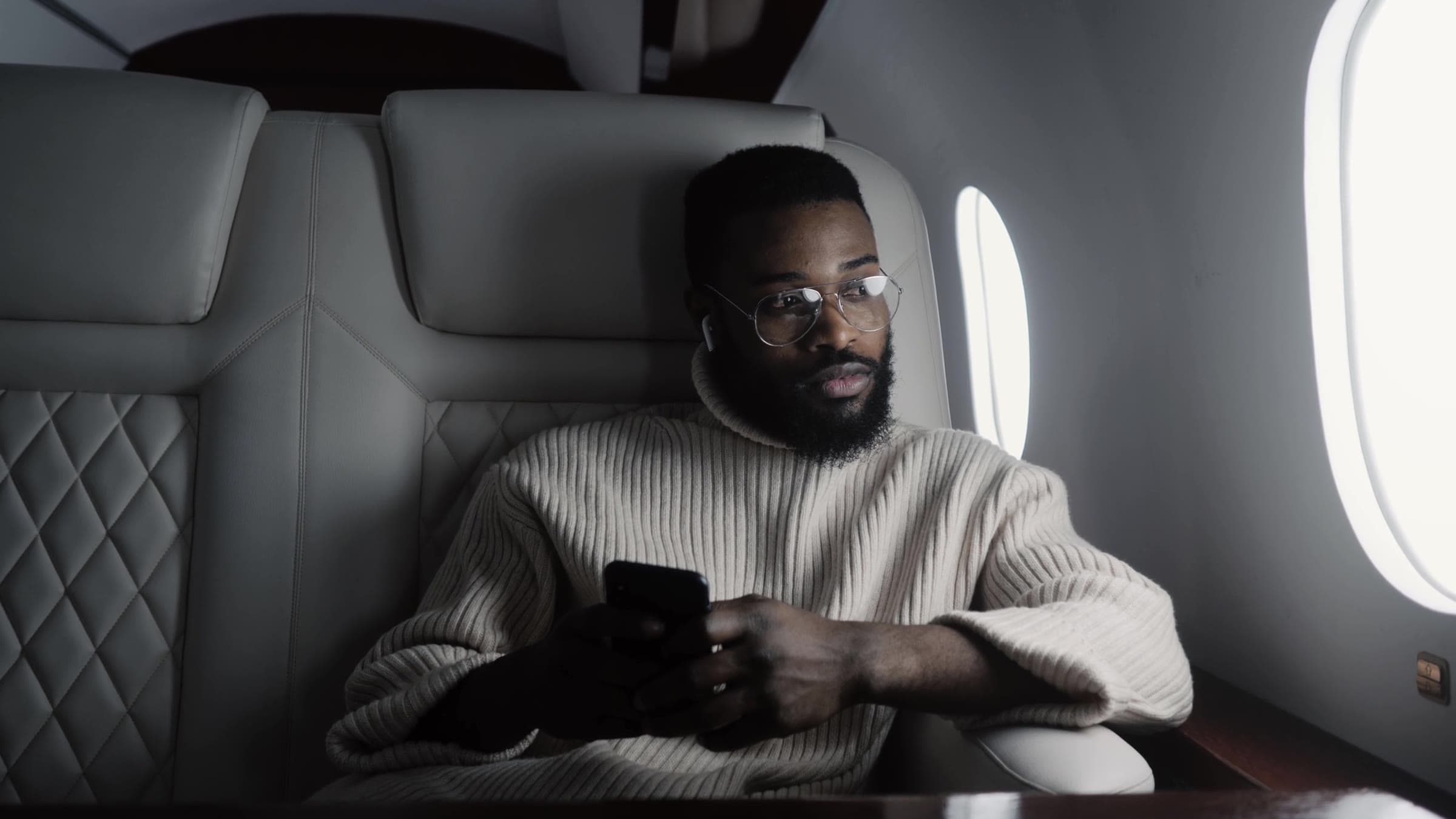 A passenger in a leather cabin seat beside an oval window