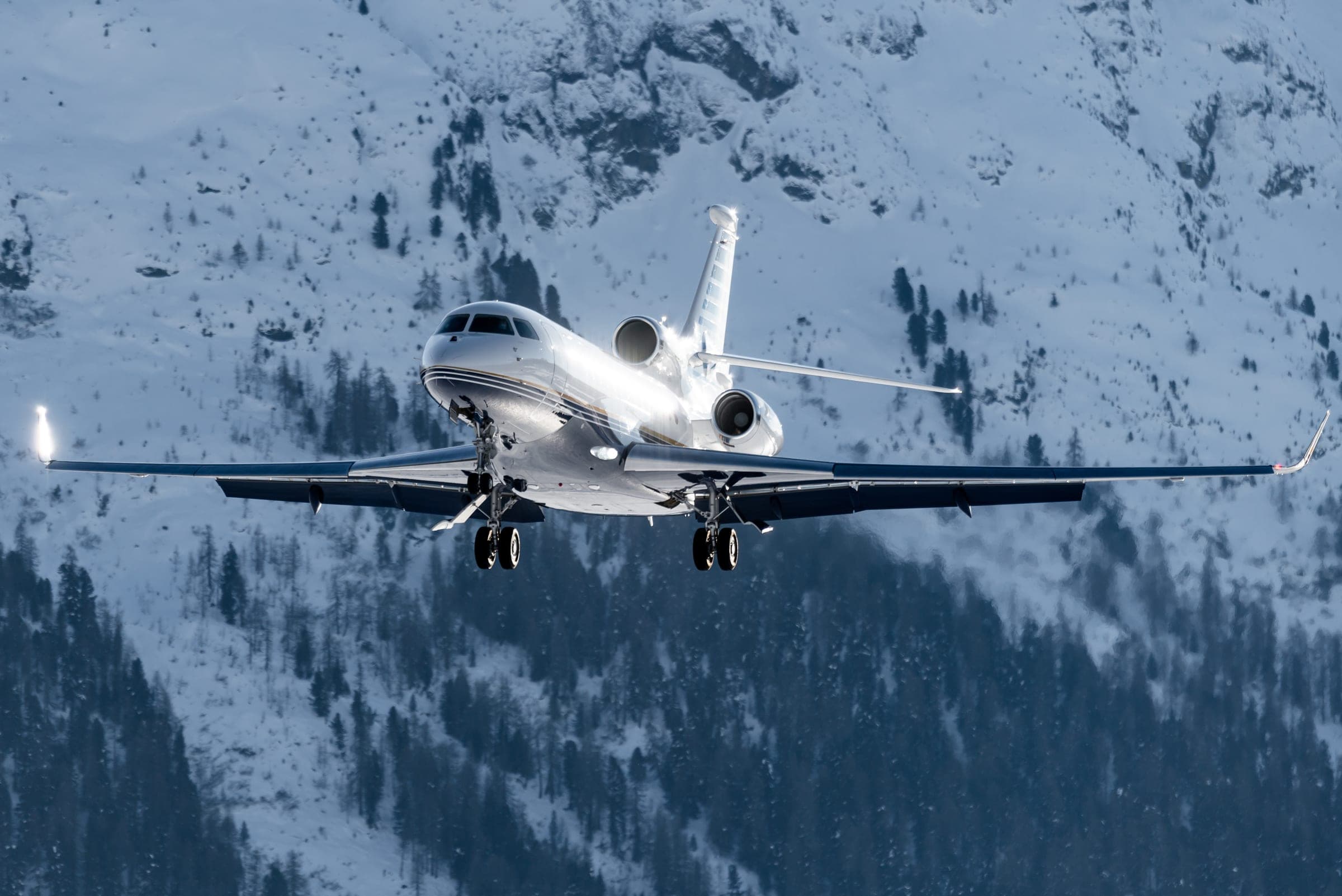 A business jet with its gear down against snowy mountains