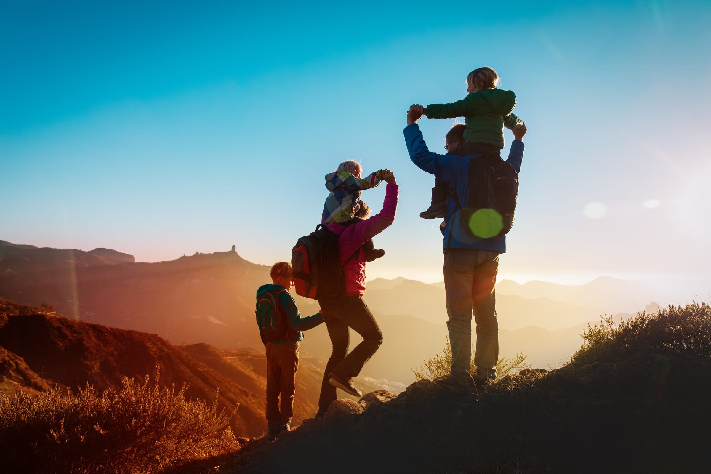 A family hiking a ridge at sunset, the youngest on a parent’s shoulders